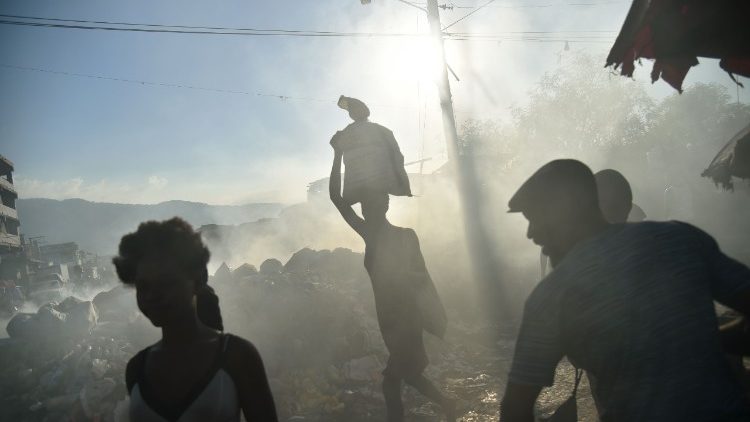 Des Haïtiens marchent à travers des poubelles fumantes, à proximité du marché de Port-au-Prince, le 20 décembre 2017.