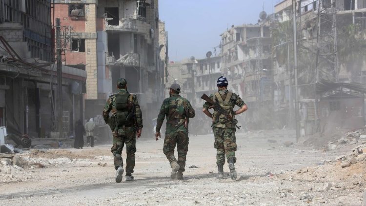 Syrian government forces walk along a ruined road in Eastern Ghouta