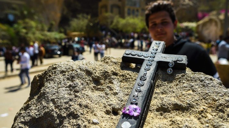 A man looks at an Egyptian Coptic cross placed on a rock
