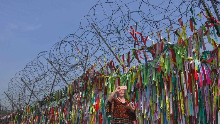 Turista tira foto junto à cerca que divide as duas Coreias, repleta de fitas com pedido de paz