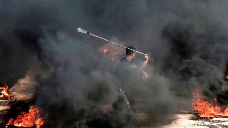 A Palestinian man uses a slingshot to throw a stone towards Israeli forces