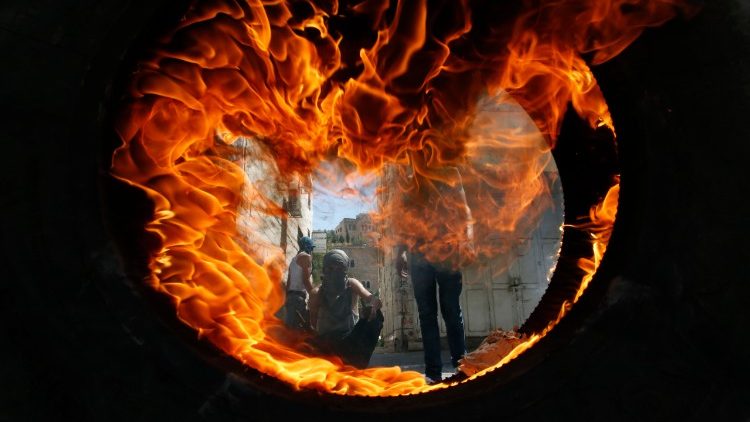 Palestinian protesters seeen through a burning tyre during clashes with Israeli soldiers in Hebron