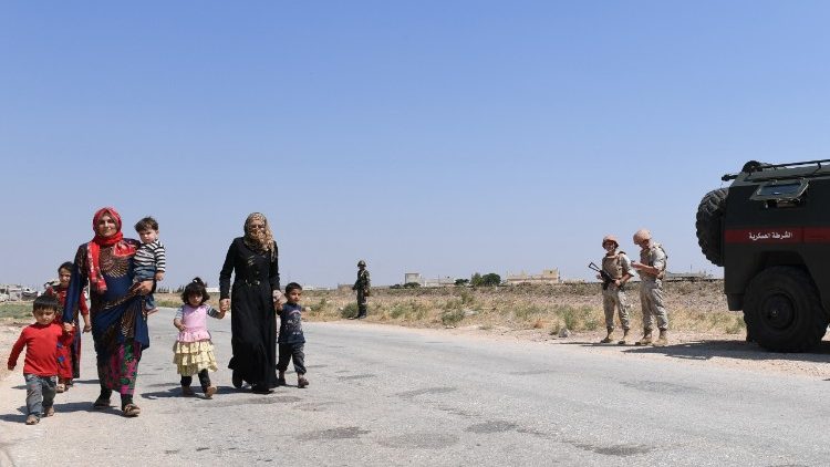 Syrian families walk as Russian and Syrian forces stand guard