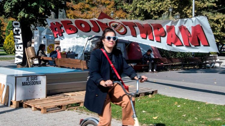A girl in Skopje rides a bicycle next to a banner reading "Boycott"