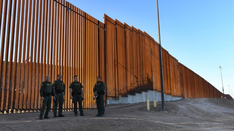 US Border Patrol Officers stand beside a completed section of the wall along the border between the United States and Mexico. 