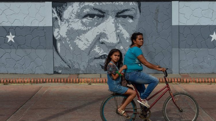 Une femme et une enfant sur un vélo devant une fresque de l'ancien président Hugo Chavez à Sabaneta de Barinas, le 21 décembre 2018.