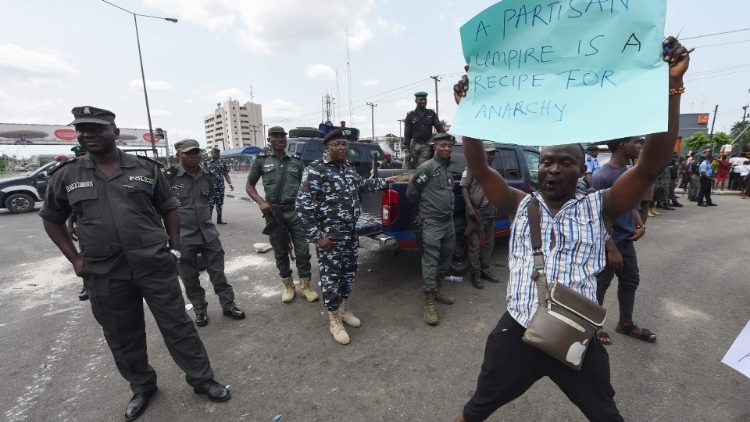 Policemen stand as a man holds a placard during a protest in Port Harcourt, Nigeria