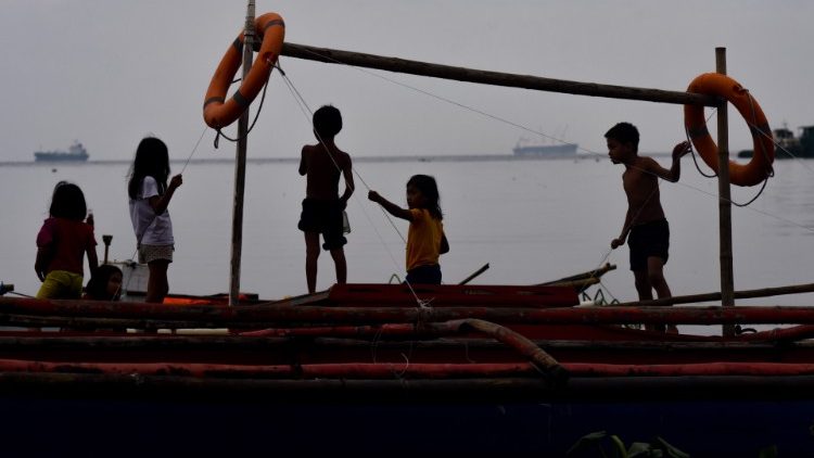 Kinder spielen an Bord eines Fischerboots am stark verschmutzten Hafen von Manila
