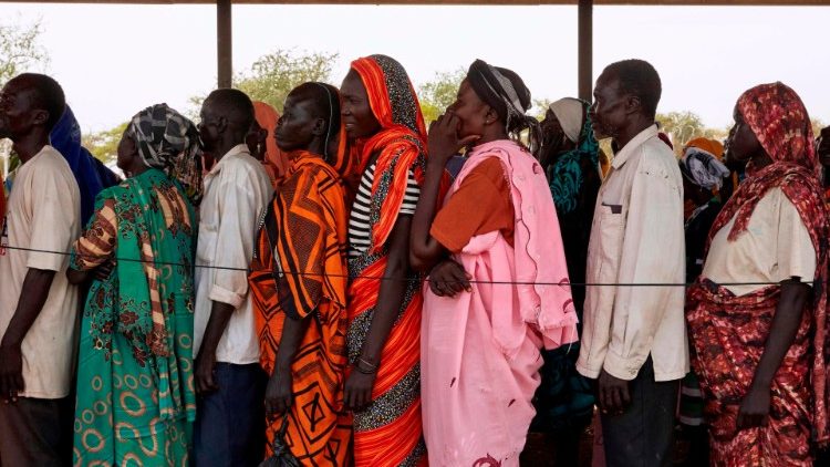 Displaced persons wait in line to receive essentials from an emergency shelter