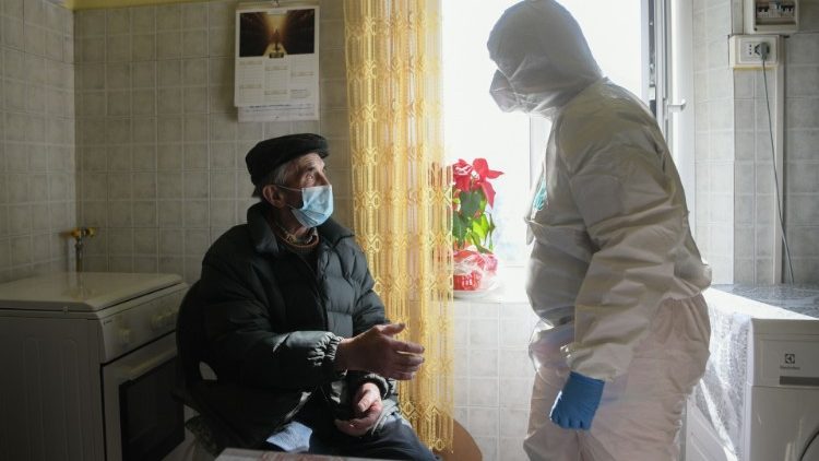 A nurse in PPE assisting an elderly man