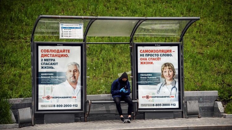 A man at a bus stop decorated with posters promoting social distancing and self-isolation in Moscow, Russia
