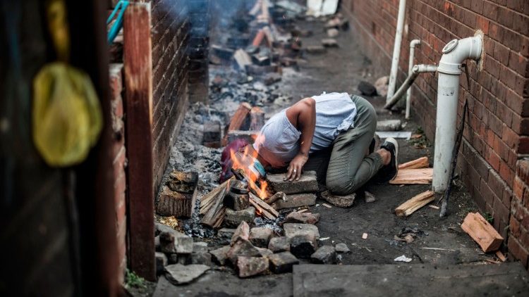 Voluntario de la ONG "El hambre no tiene religión" sopla debajo de una olla para encender un fuego para cocinar gachas para el desayuno para niños en áreas desfavorecidas en el suburbio de Westbury, en Johannesburgo.