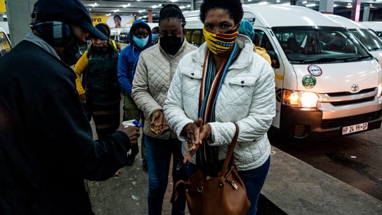A taxi attendant in SA sprays commuters with hand sanitiser while they queue at a taxi rank