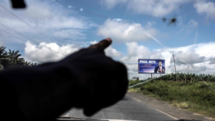 (File) Taxi driver points towards an electoral poster where the road crosses into Buea, an anglophone region of Cameroon.