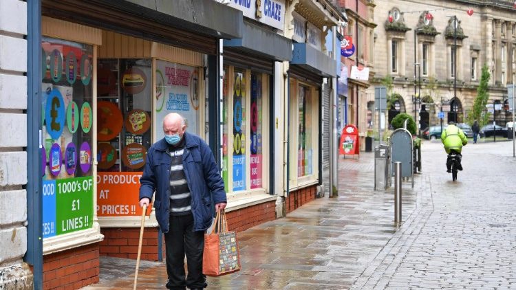 An elderly man wearing a face mask walks past shops