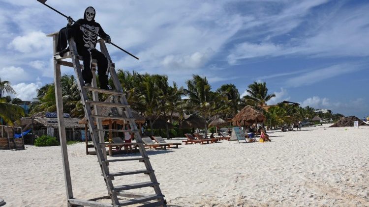 A man dressed as the Grim Reaper warns beachgoers in Mexico to return home
