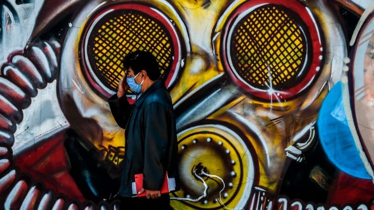 A Colombian man wears a facemask as he passes a mural in Bogota