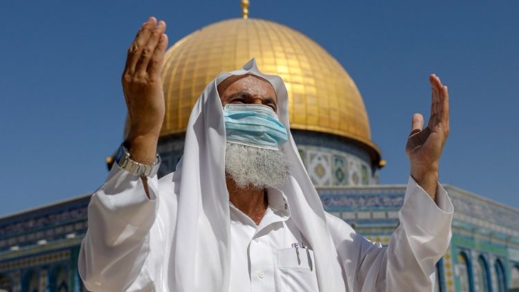 Homem palestino em oração diante de uma mesquita