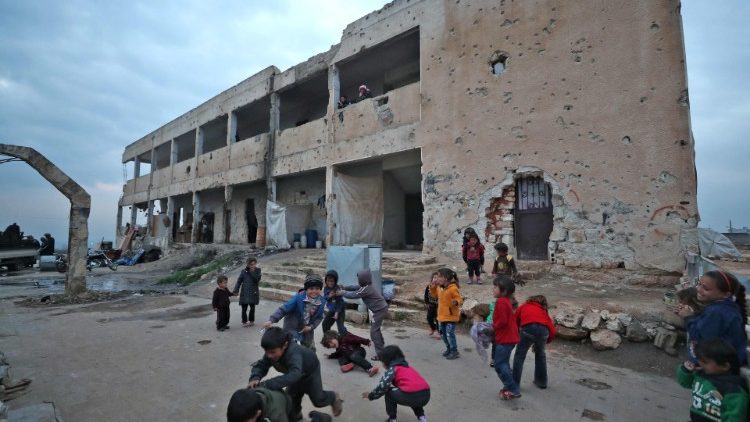 Filhos de famílias deslocadas brincam diante do que foi uma escola antes da guerra