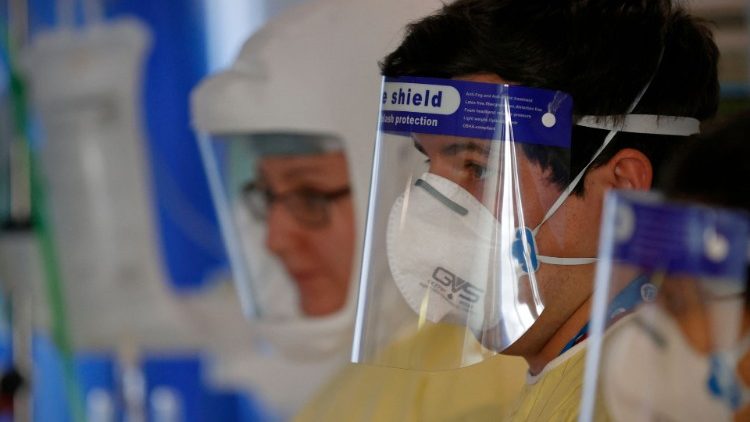 A firefighter wearing a face shield helps health care workers with a patient in a Covid-19 ICU unit