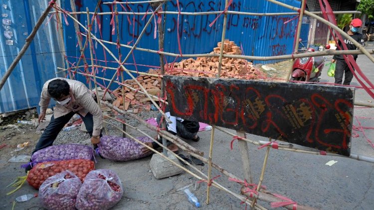 Pessoas que vivem na zona vermelha obtêm produtos frescos por meio de uma barricada criada como parte das restrições de bloqueio introduzidas para tentar impedir um aumento de casos do coronavírus. (Foto de TANG CHHIN Sothy / AFP)