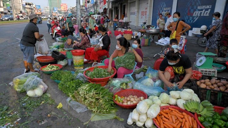 Vendedores preparam vegetais para venda ao longo de uma rua enquanto os mercados permaneciam fechados em meio a restrições introduzidas para tentar impedir um aumento de casos do coronavírus. (Foto por TANG CHHIN Sothy / AFP)