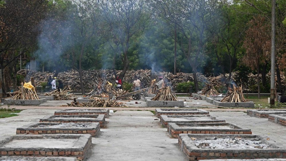 Trabalhadores são vistos em meio a piras funerárias em chamas de pessoas que morreram devido ao coronavírus Covid-19 em um local de cremação em Nova Delhi em 17 de maio de 2021. (Foto de Sajjad HUSSAIN / AFP)