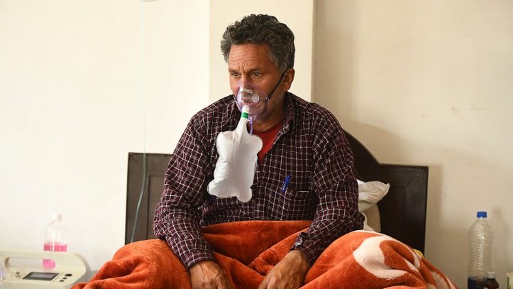 श्रीनगर के कोविड-19 स्वास्थ्य केंद्र के बेड पर बैठा एक मरीज