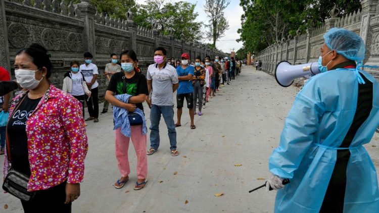 Um soldado (dir) dá instruções enquanto as pessoas fazem fila para receber a segunda dose da vacina contra o coronavírus Sinopharm  da China, em Phnom Penh. (Foto de TANG CHHIN Sothy / AFP)