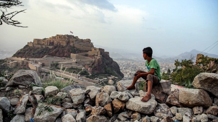 Menino iemenita olhando para a bandeira do seu país, hasteada em um monumento do século XII em al-Qahira, Iêmen