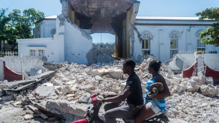 People pass in front of the rubble from a destroyed wall outside of the "Sacre Coeur de Cayes" church in Les Cayes