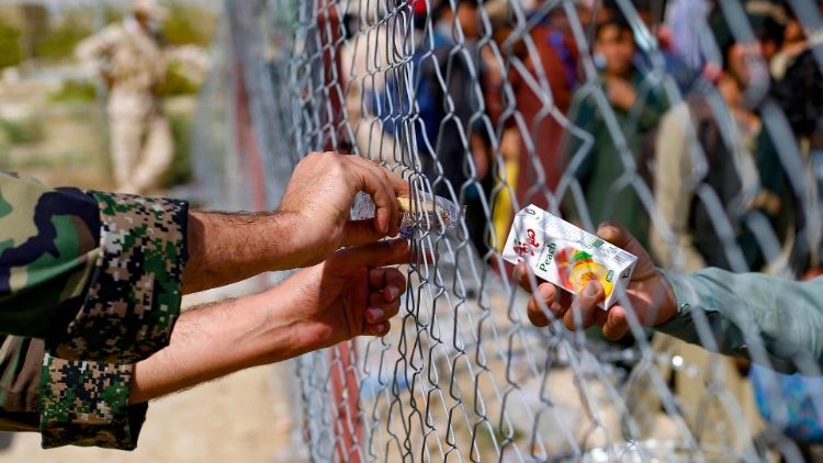 Ein iranischer Soldat versorgt Flüchtlinge aus Afghanistan durch einen Zaun hindurch mit Getränken 