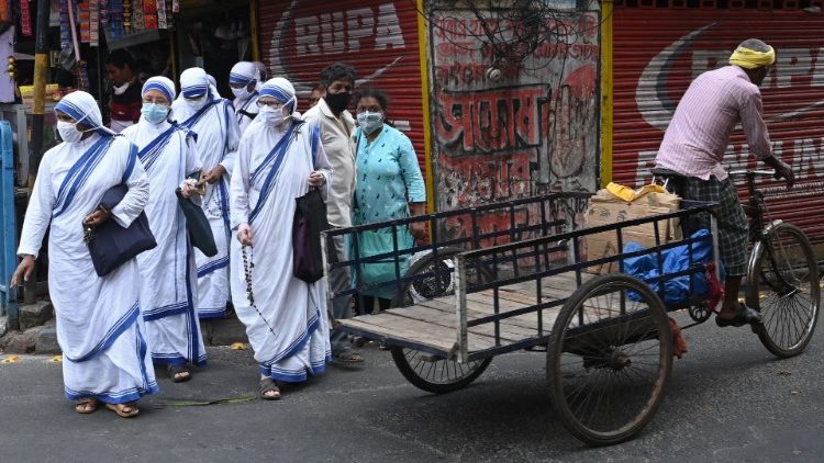 Missionárias da Caridade protegidas por máscara caminham por rua de Calcutá. (Foto de Dibyangshu SARKAR)