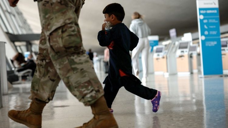 Menino afegão caminha ao lado de militar dos EUA enquanto ele e sua família são conduzidos pelo Aeroporto Internacional de Dulles, Virgínia, para embarcar em um ônibus que os levará a um centro de processamento de refugiados.