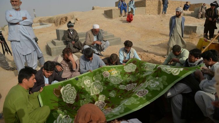 Relatives and friends of one of the victims of Friday's bombing of a Shiite Mosque hold a blanket over his grave in Kunduz
