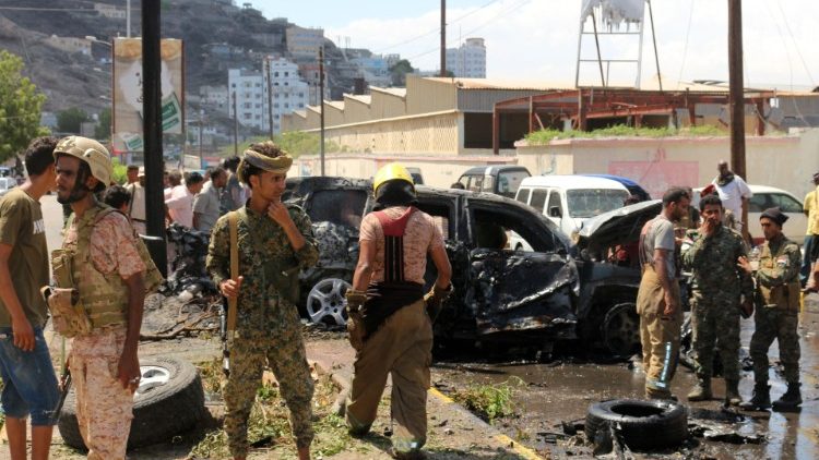 Yemeni security forces and rescue teams stand around a burnt car following an explosion that hit the city of Aden on Sunday