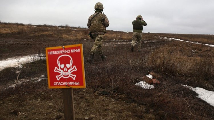 Ukrainian Military Forces servicemen walk past a metal plate which reads "caution mines" on the frontline with Russia-backes separatists, January 11