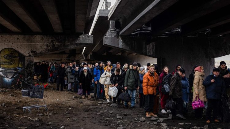 Evacuees stand under a destroyed bridge as they flee the city of Irpin, northwest of Kyiv, 7 March
