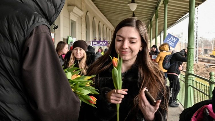 अंतरराष्ट्रीय महिला दिवस के अवसर पर पोलैंड में एक पुरोहित के हाथ से फूल मिलने पर मुस्कुराती एक महिला