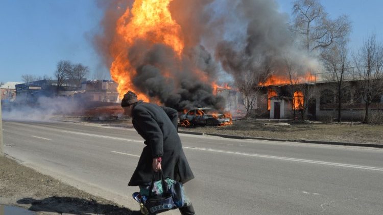 Ucraina. Un anziano si allontana lungo una strada di Kharkiv, sullo sfondo le fiamme causate da tiri di artiglieria russa