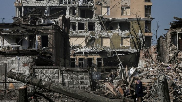 Um casal caminha em frente a casas destruídas por bombardeios em Kharkiv em 25 de março de 2022, durante a invasão militar da Rússia lançada na Ucrânia. - Ataques russos contra uma instalação médica em Kharkiv. (Foto: Aris Messinis/AFP)