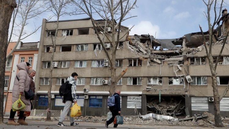 People walk past a damaged building in the Ukrainian city of Mykolaiv on March 27, 2022. - For three weeks, 13-year-old Sofia has been stuck in bed in the basement of a hospital in the southern Ukrainian city of Mykolaiv undergoing three operations that have still not removed all the shrapnel from her skull. (Photo by Oleksandr GIMANOV / AFP)