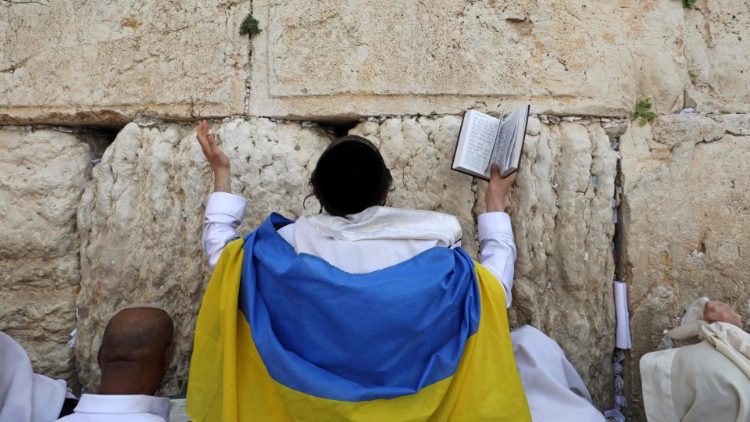 Um judeu envolto em uma bandeira ucraniana participa da oração Cohanim (bênção do padre) durante o feriado da Páscoa no Muro das Lamentações, na Cidade Velha de Jerusalém, em 18 de abril de 2022. (Foto de GIL COHEN-MAGEN / AFP)