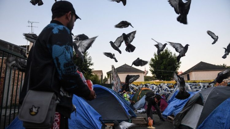 Aux abords d'un camp de réfugiés en banlieue parisienne. Deux personnes afghanes nourrissent les pigeons. 11 mai 2022. 