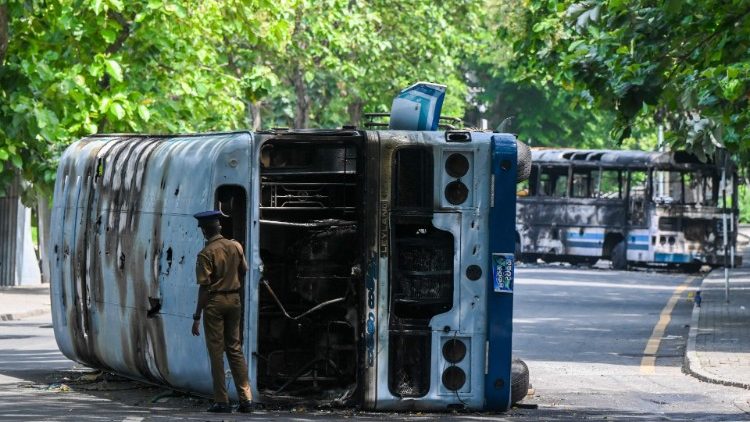 Un poliziotto ispeziona un autobus data alle fiamme durante le proteste antigovernative a Colombo (Ishara Kodikara / Afp)
