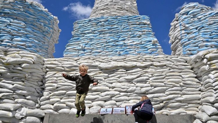 Crianças brincam no Monumento à Princesa Olga, Santo André Apóstolo e os Educadores Cirilo e Metódio, protegidos por sacos de areia, no centro da capital ucraniana de Kyiv, em 28 de maio de 2022. (Foto de Sergei SUPINSKY/AFP)