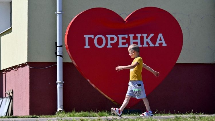 Menino passa por uma placa que diz "Eu amo Gorenka". Moradores de cidades satélites de Kiev estão superando traumas da ocupação russia e depositando esperança na reconstrução.