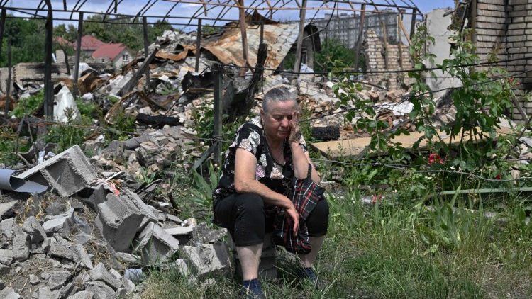 Kateryna, 70, espera com outros moradores locais por ajuda humanitária ao lado de uma casa destruída ao longo de uma rua na cidade de Bucha, a noroeste da capital ucraniana de Kyiv, em 16 de junho de 2022, quando a guerra russo-ucraniana entra em seu 113º dia. (Foto de Genya SAVILOV/AFP)