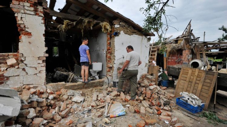 Pessoas removem destroços de uma casa, destruída durante a invasão russa da Ucrânia na vila de Pidgayne, região de Kiev, em 9 de julho de 2022. (Foto de Sergei CHUZAVKOV / AFP)