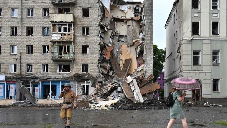 Um morador local passa por um socorrista ucraniano que trabalha do lado de fora de um prédio parcialmente destruído após um ataque de mísseis russos em Kharkiv em 11 de julho de 2022, em meio à invasão militar da Rússia lançada na Ucrânia. (Foto de SERGEY BOBOK/AFP)
